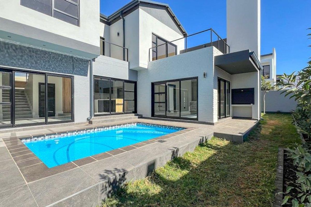 Modern rear exterior featuring a swimming pool, tiled patio area, built-in braai, and large sliding glass doors connecting to the home's interior living spaces.