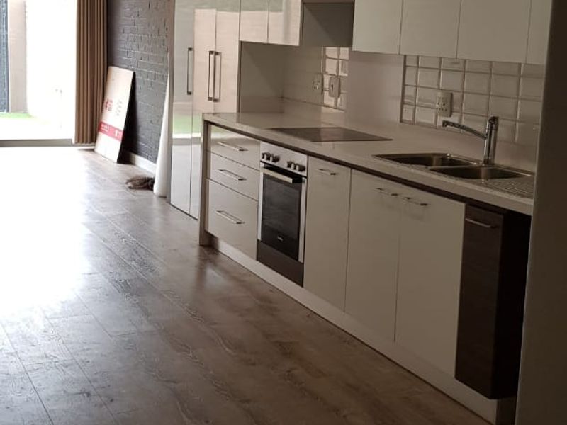 Modern kitchen featuring sleek white cabinetry, integrated appliances, a tiled backsplash, and an exposed brick wall, leading to an outdoor patio area.