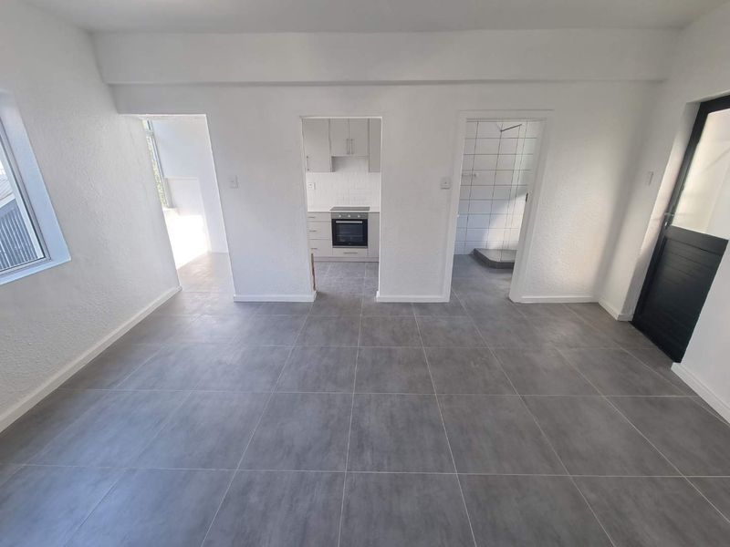 An open-plan living area featuring modern grey floor tiles, with direct access to a compact kitchen and a tiled bathroom.