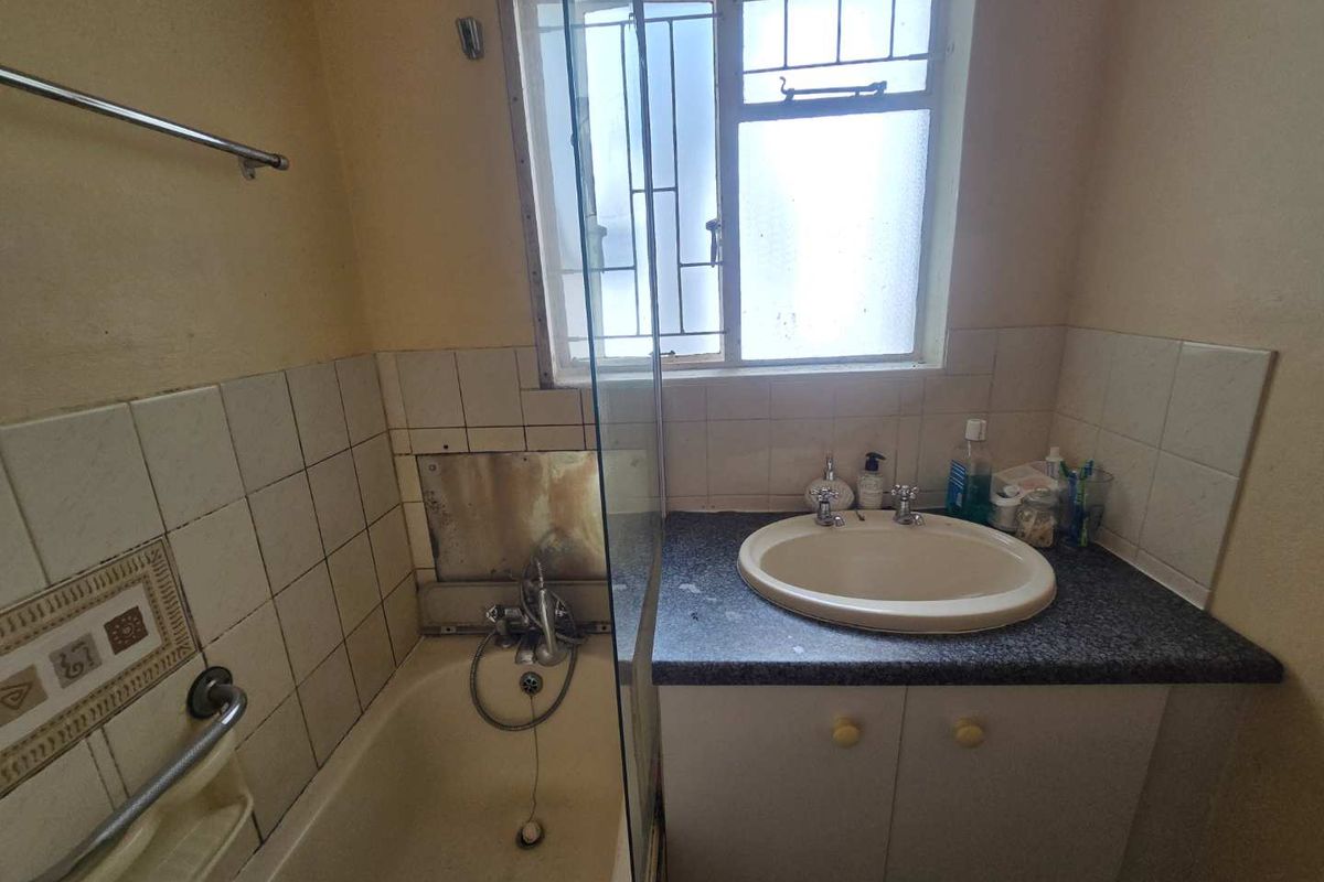 A dated bathroom featuring a built-in vanity with drop-in basin, a bathtub with shower screen, and tiled splashbacks requiring maintenance or renovation.
