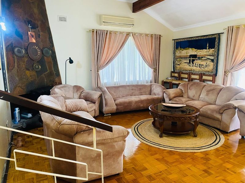 Spacious living room featuring classic parquet flooring, a prominent stone fireplace, and an exposed timber beam, offering a warm and traditional atmosphere.