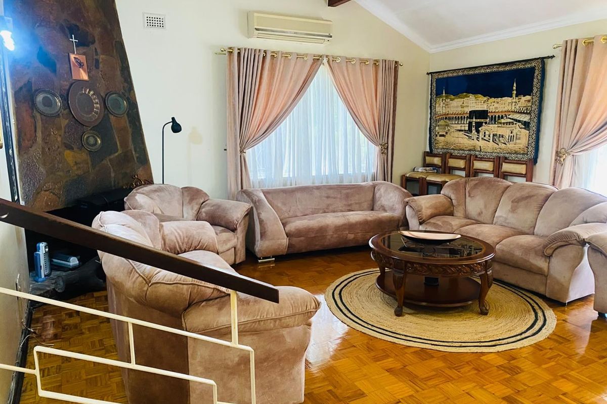 Spacious living room featuring classic parquet flooring, a prominent stone fireplace, and an exposed timber beam, offering a warm and traditional atmosphere.