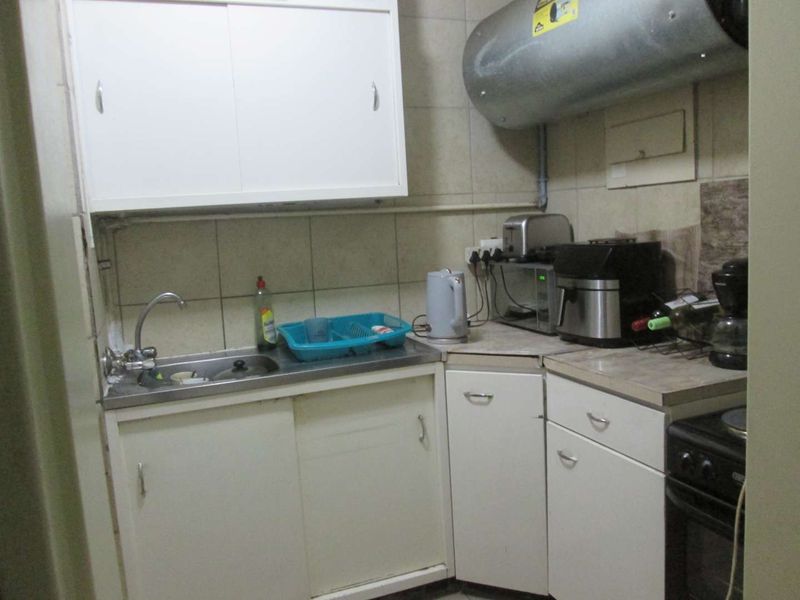 Compact kitchen featuring basic cabinetry, tiled splashback, stainless steel sink, and an exposed electric water heater.