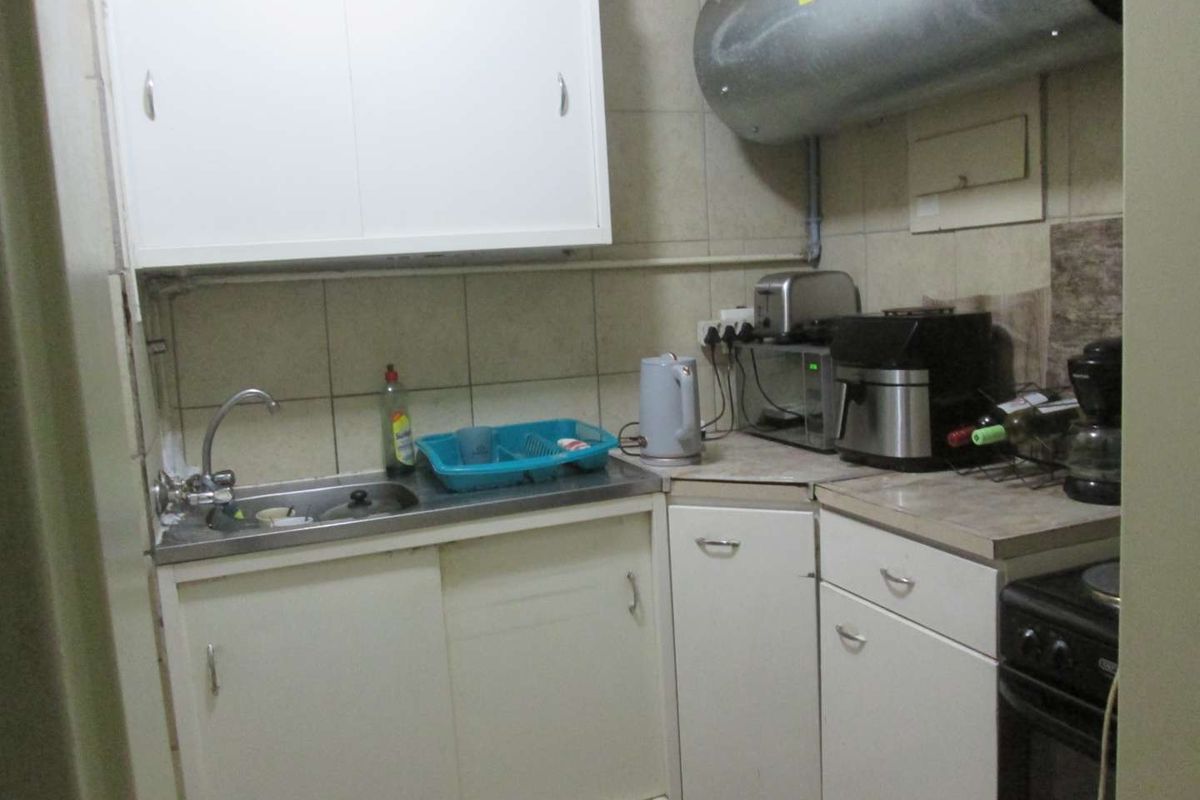 Compact kitchen featuring basic cabinetry, tiled splashback, stainless steel sink, and an exposed electric water heater.