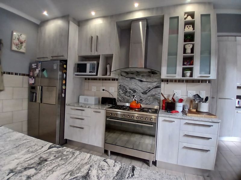Modern kitchen featuring light wood-grain cabinetry, stone countertops, a stone splashback, and a stainless steel gas stove with an integrated extractor fan.