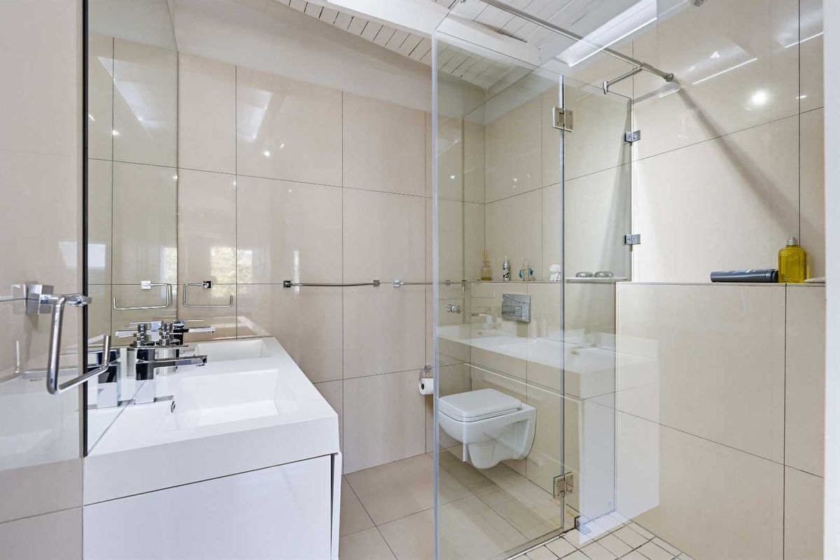 Modern bathroom featuring a wall-mounted toilet, glass shower enclosure, and a sleek built-in vanity with contemporary fixtures and neutral tiling.