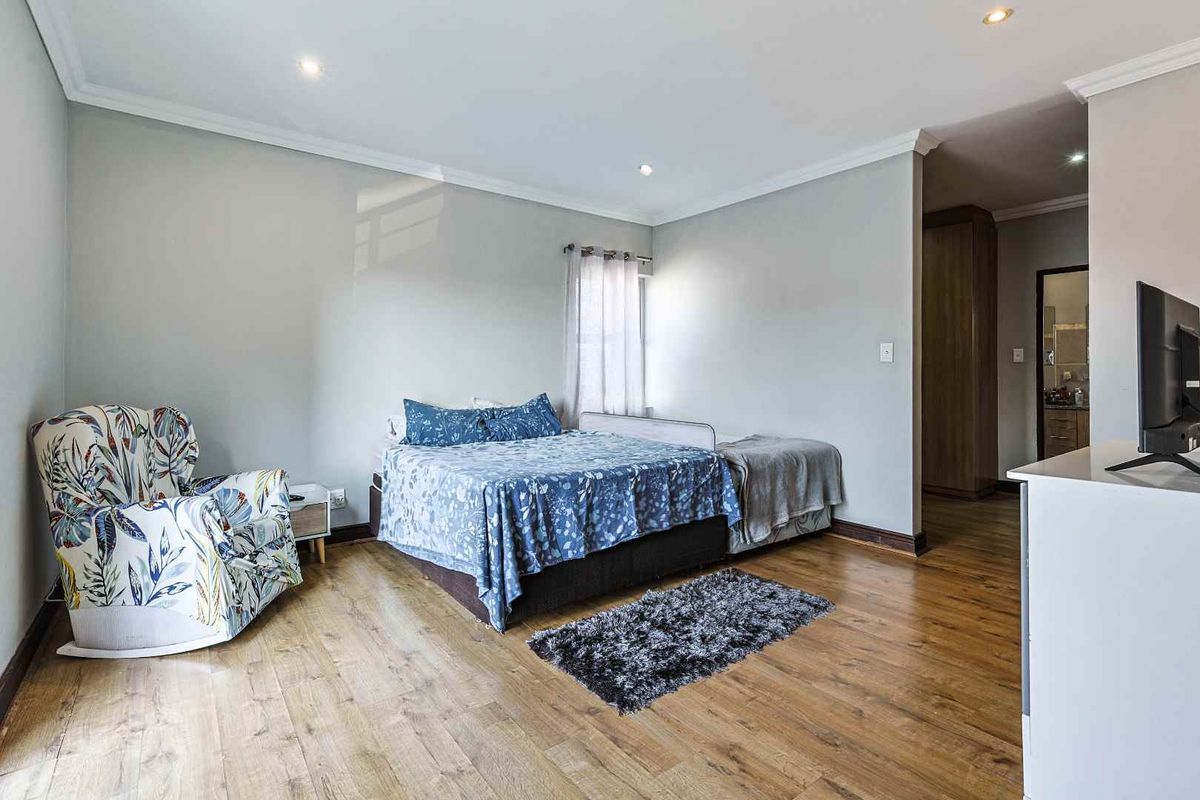 A well-maintained bedroom featuring laminate flooring, recessed downlighting, and built-in storage, with an adjoining en-suite bathroom area.