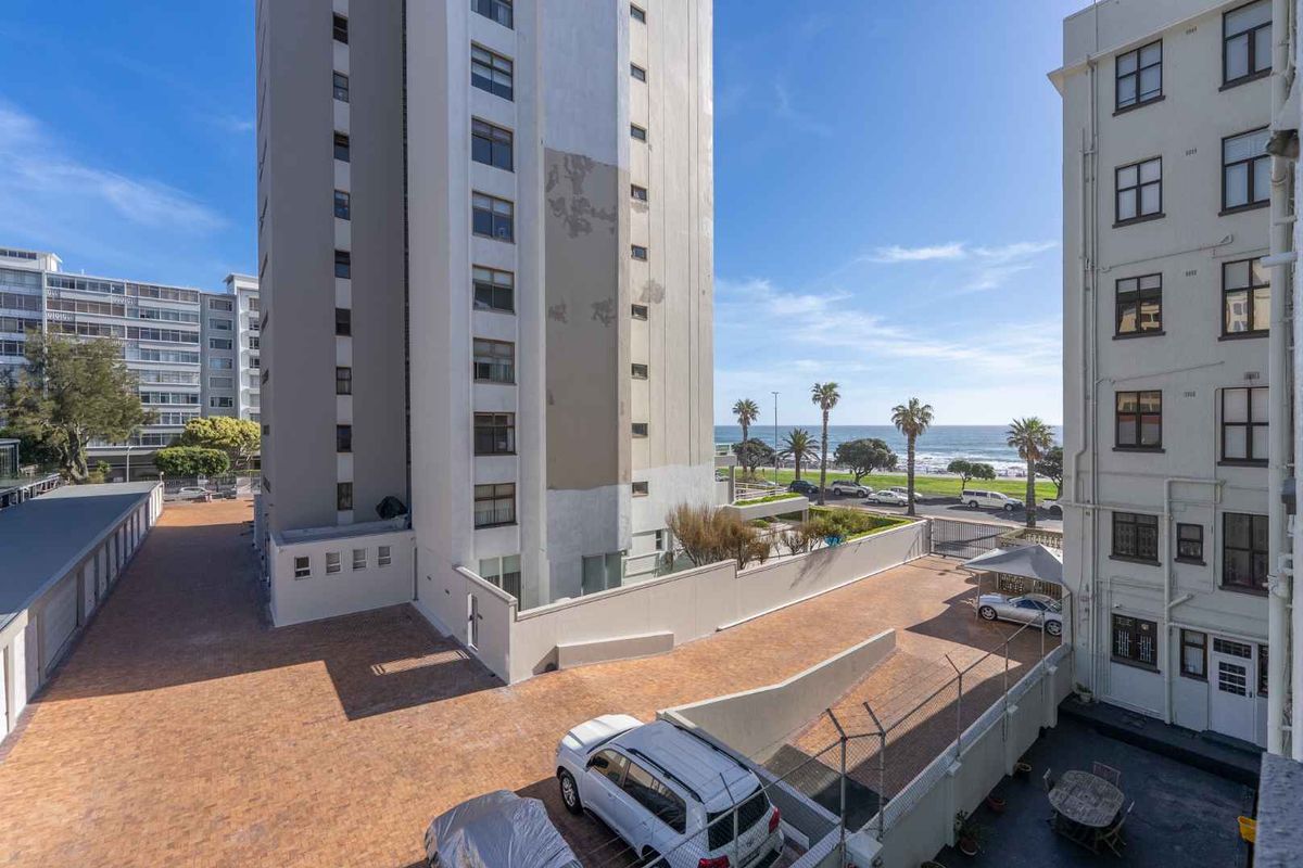 An elevated view of the apartment complex rear exterior, featuring a paved driveway, perimeter fencing, and visible building facade maintenance requirements.