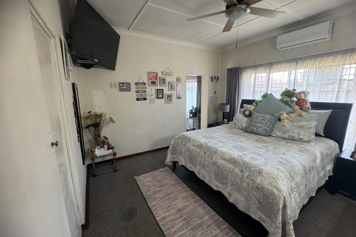 A bedroom featuring a wall-mounted air conditioning unit, ceiling fan, and carpeted flooring with access to an adjacent room.