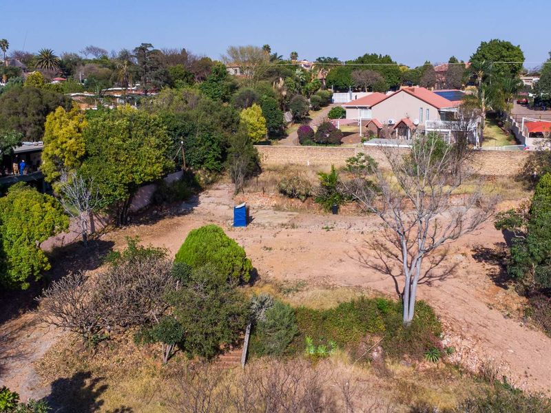 An aerial view of a vacant residential plot featuring mature trees and established boundary walls in a suburban setting.