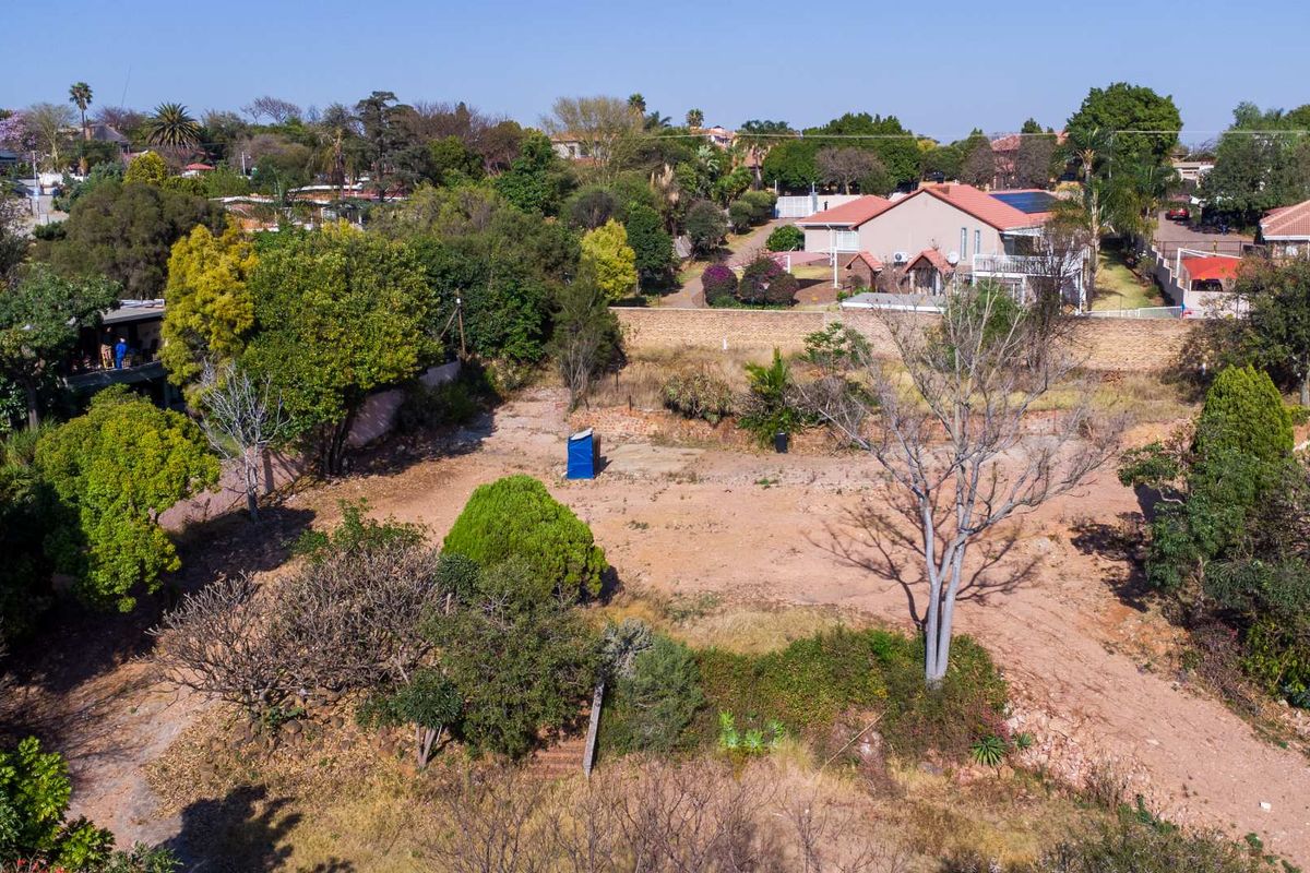 An aerial view of a vacant residential plot featuring mature trees and established boundary walls in a suburban setting.