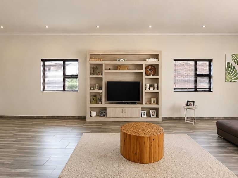 Spacious living room featuring a large built-in media unit, modern tiled flooring, recessed lighting, and dual windows with venetian blinds.