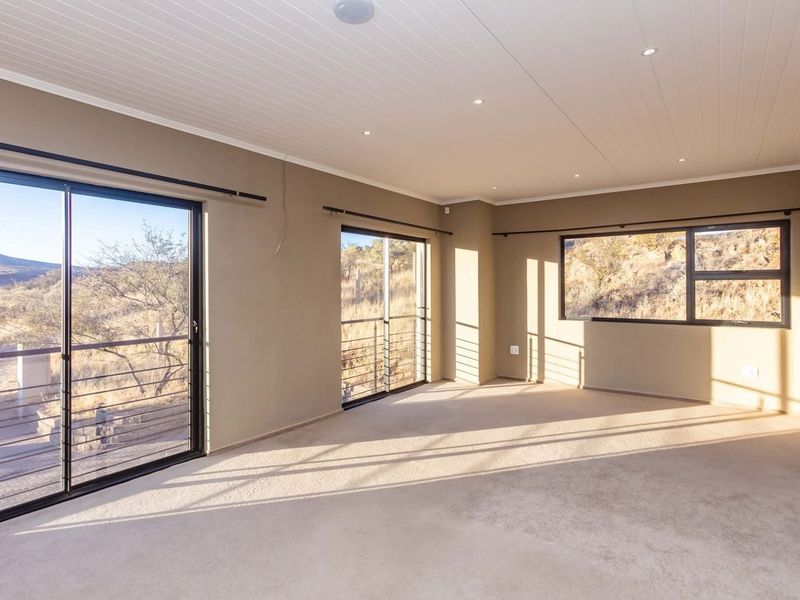 A spacious, empty living room featuring neutral carpeting, recessed lighting, and large sliding glass doors that offer expansive views of the surrounding landscape.