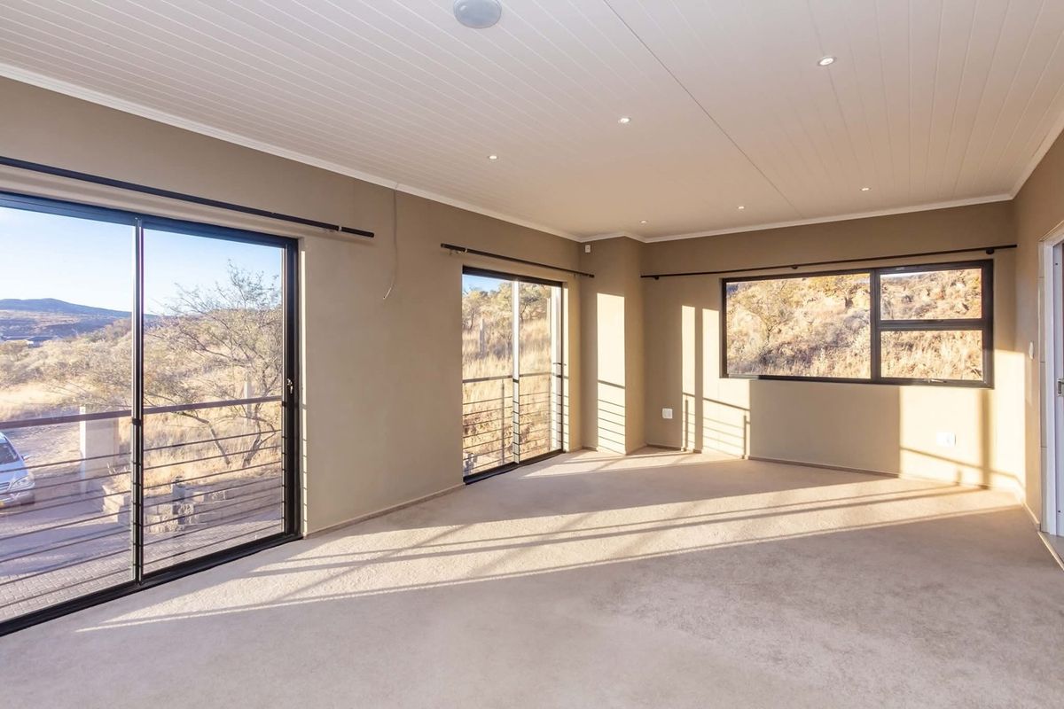 A spacious, empty living room featuring neutral carpeting, recessed lighting, and large sliding glass doors that offer expansive views of the surrounding landscape.