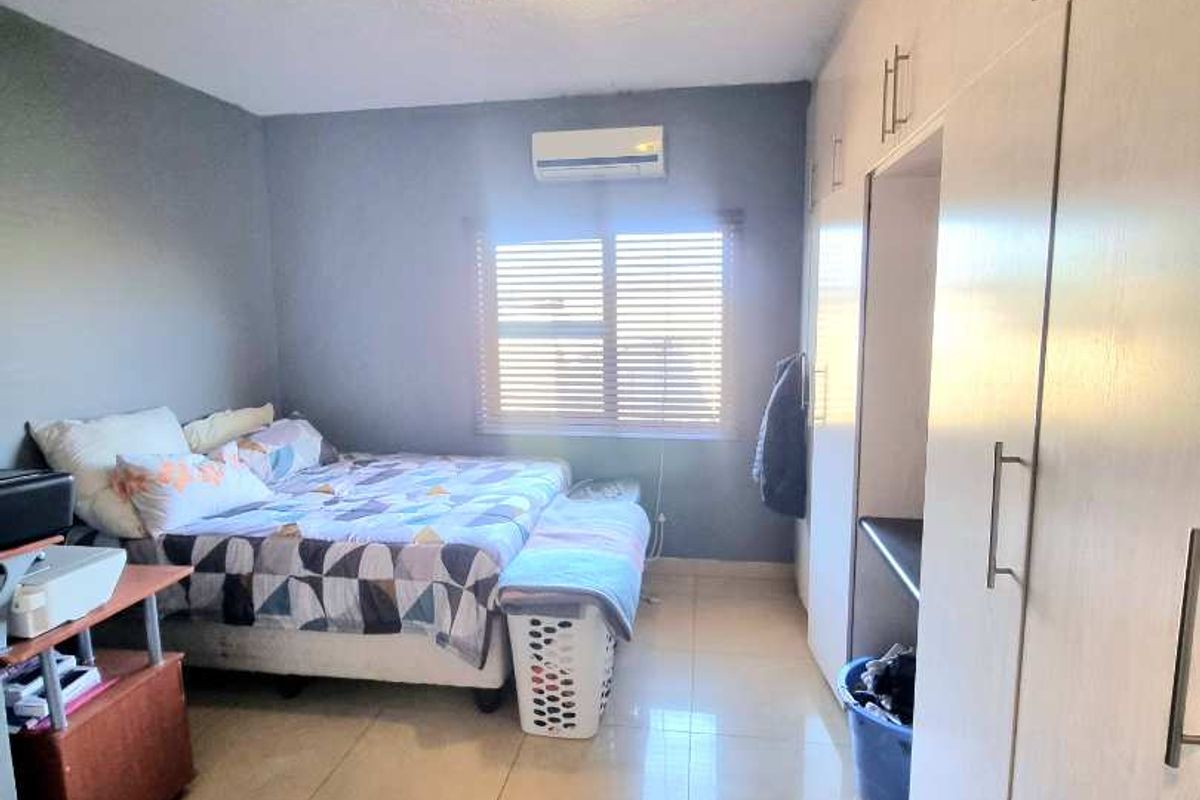 A functional bedroom featuring built-in floor-to-ceiling wardrobes, tiled flooring, and a wall-mounted air conditioning unit.