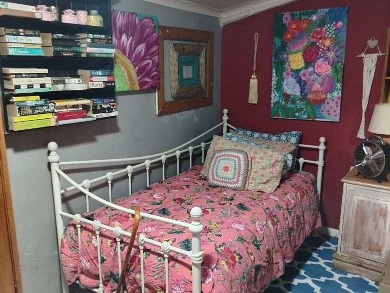 A compact bedroom featuring tiled flooring, built-in shelving, and a panelled ceiling, currently decorated with a vibrant aesthetic.