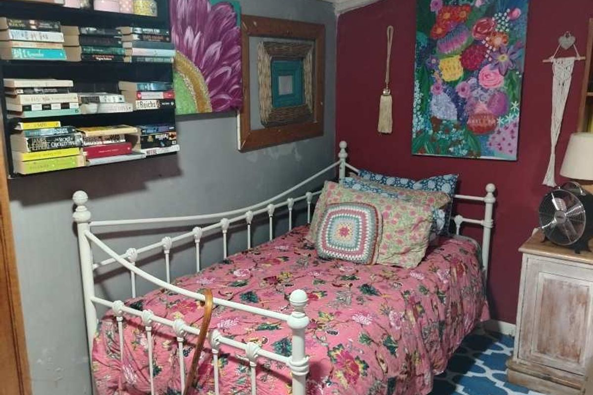 A compact bedroom featuring tiled flooring, built-in shelving, and a panelled ceiling, currently decorated with a vibrant aesthetic.