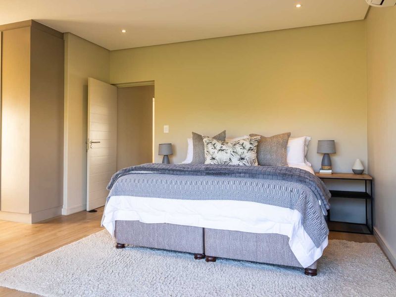 A well-maintained bedroom featuring neutral walls, laminate flooring, built-in cupboards, and recessed downlighting.