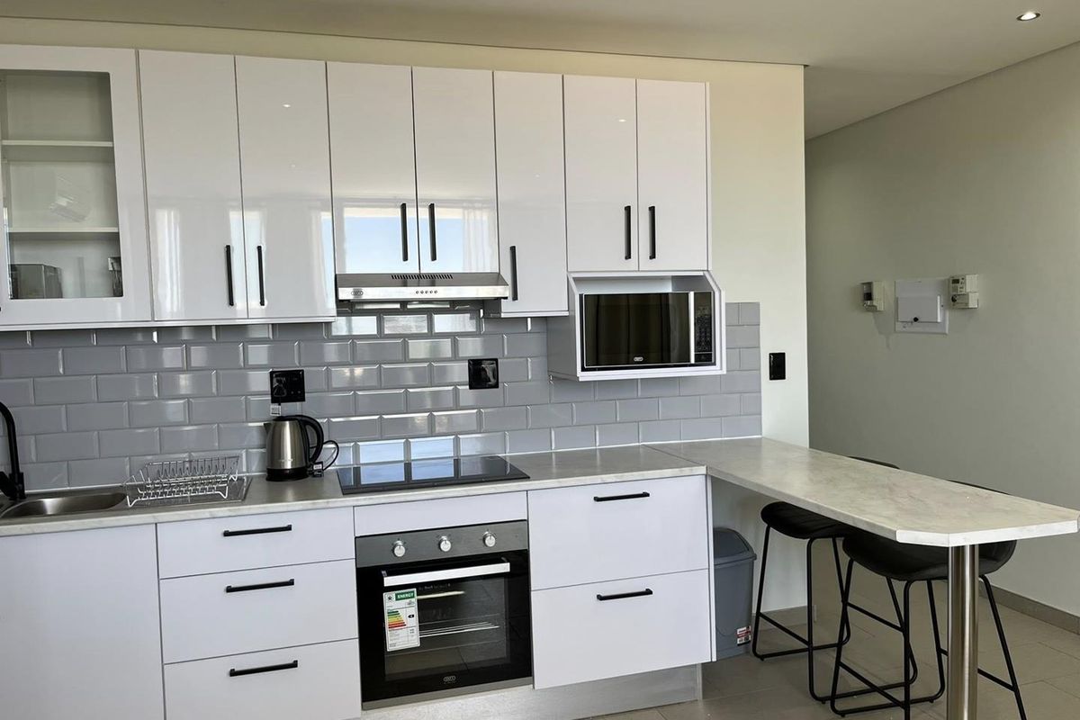 Modern kitchen featuring white gloss cabinetry, grey subway tile backsplash, integrated appliances, and a convenient breakfast bar with stone-look countertop.