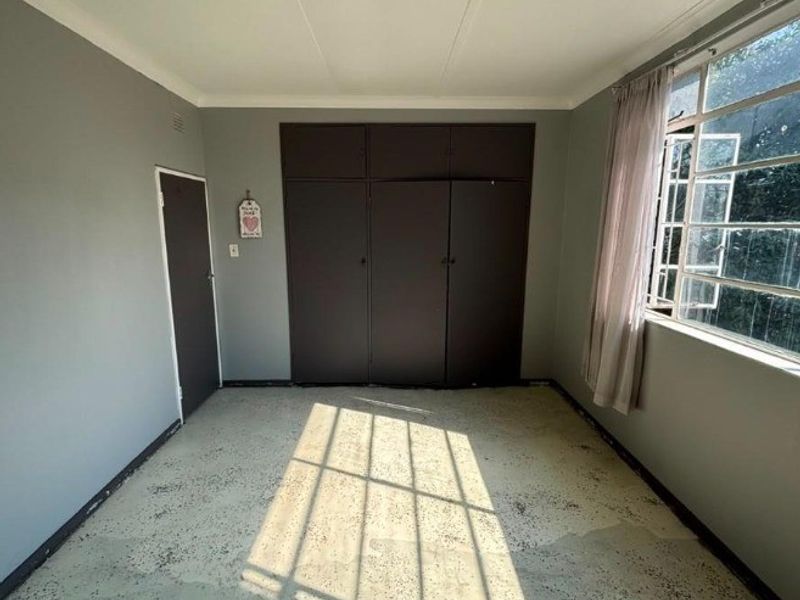 A vacant bedroom featuring built-in cupboards, grey painted walls, and a large steel-framed window allowing natural light.