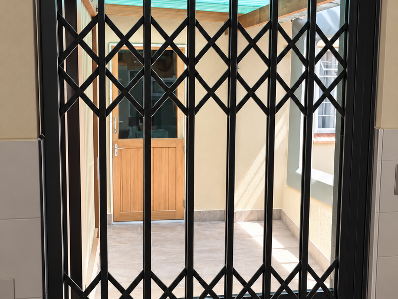 A covered patio area featuring tiled flooring, a timber door, and a secure metal gate, providing a protected outdoor transition space.