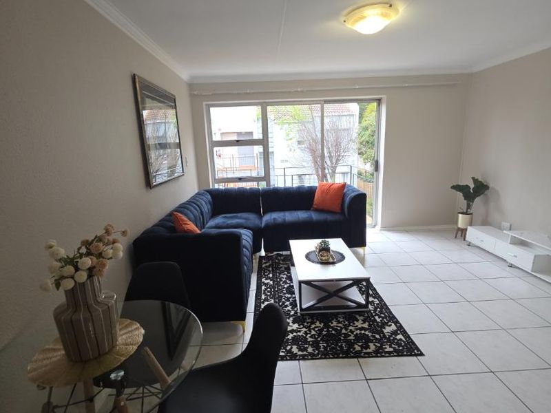 A bright, open-plan living area featuring neutral tiled flooring and a large sliding glass door that provides access to an outdoor balcony.