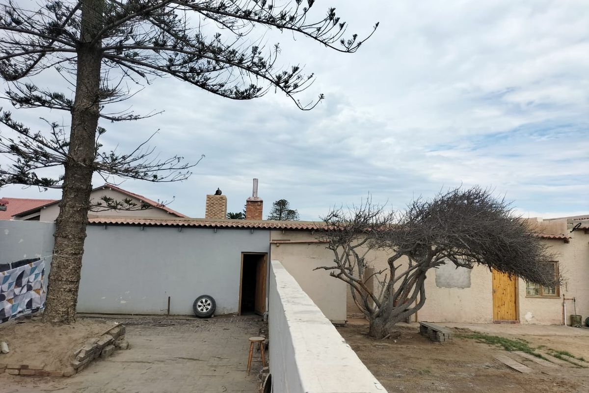 Rear exterior view of the property featuring a concrete courtyard, boundary wall, and brick chimneys.