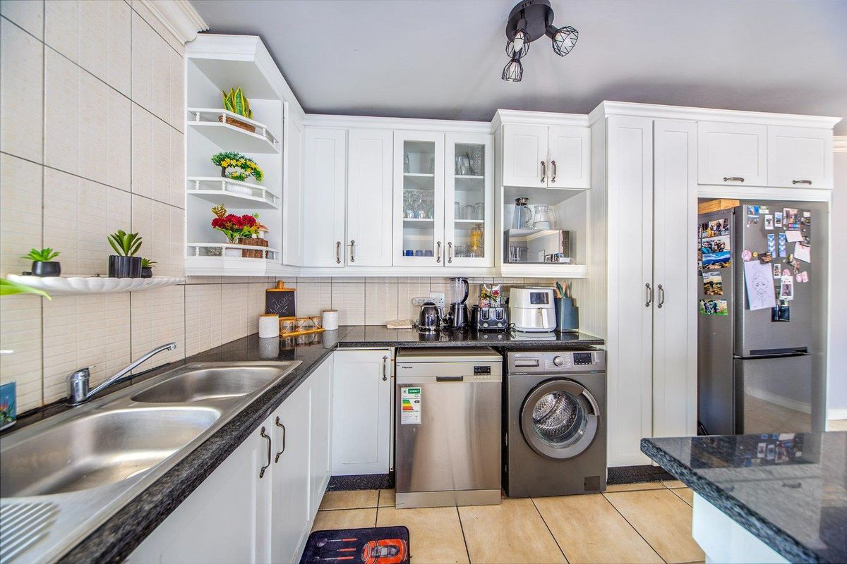 A well-maintained kitchen featuring white cabinetry, granite countertops, a double basin sink, and tiled flooring with integrated shelving and modern lighting.