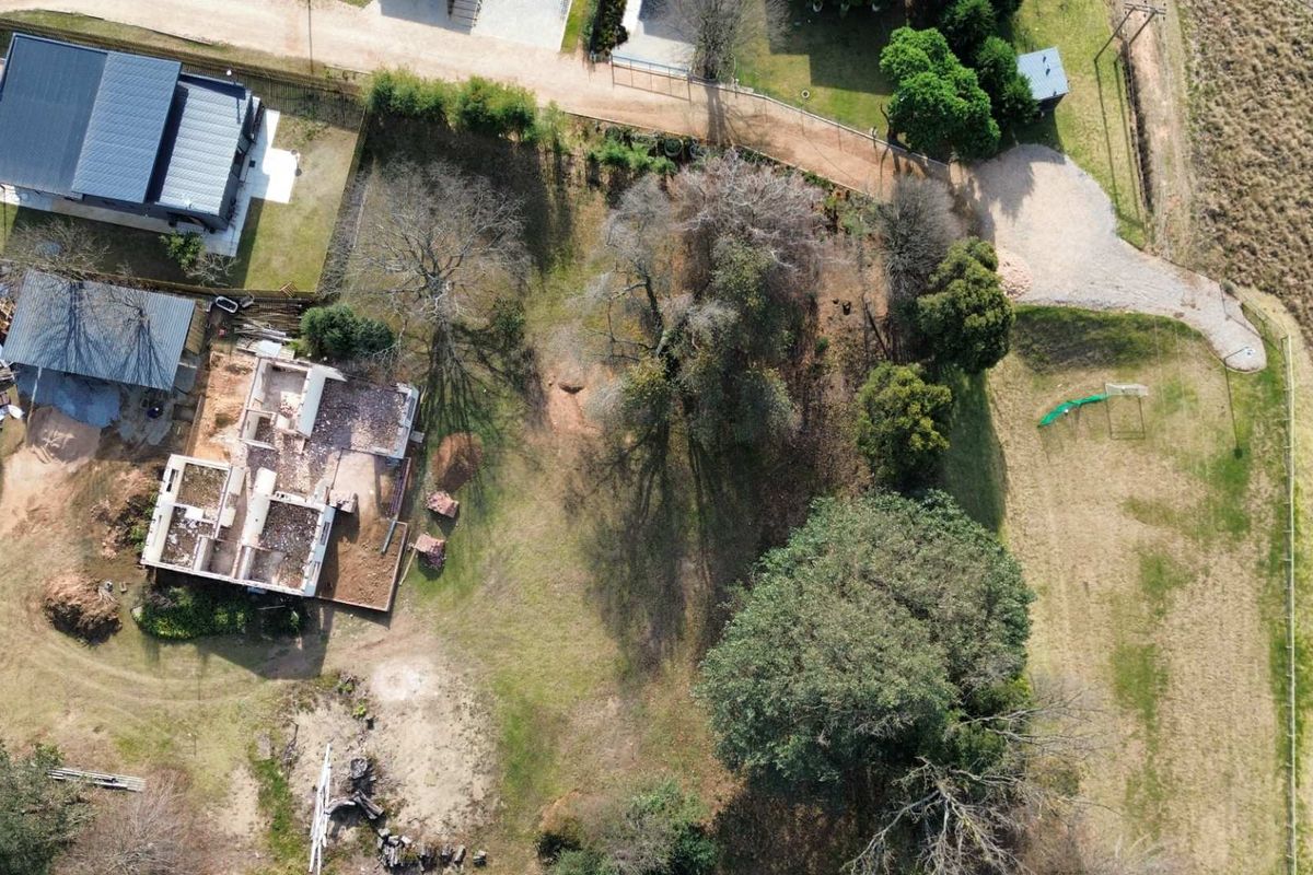 Aerial view of a residential plot featuring a partially constructed building, mature trees, and open land area.