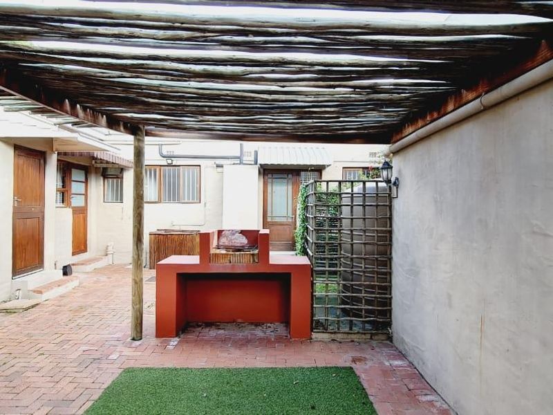 Outdoor patio area featuring a built-in braai, brick paving, and a rustic timber pergola, providing a functional space for outdoor entertaining.