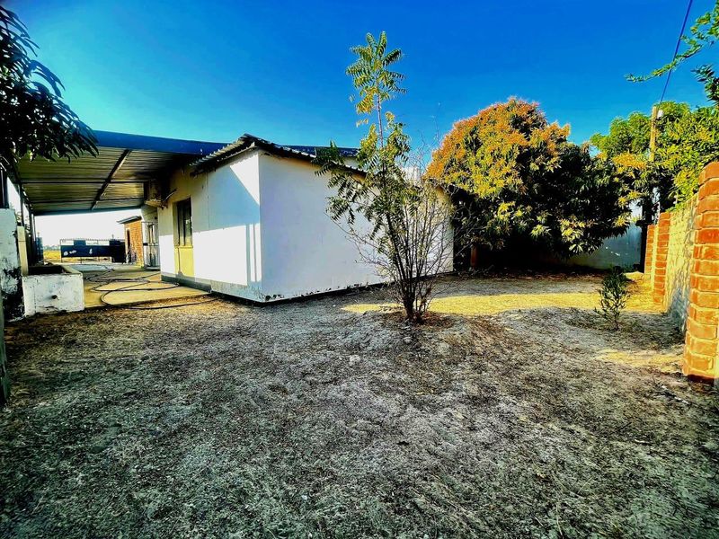 Rear exterior view of the property featuring a corrugated metal roof extension, brick boundary wall, and an unlandscaped yard area.