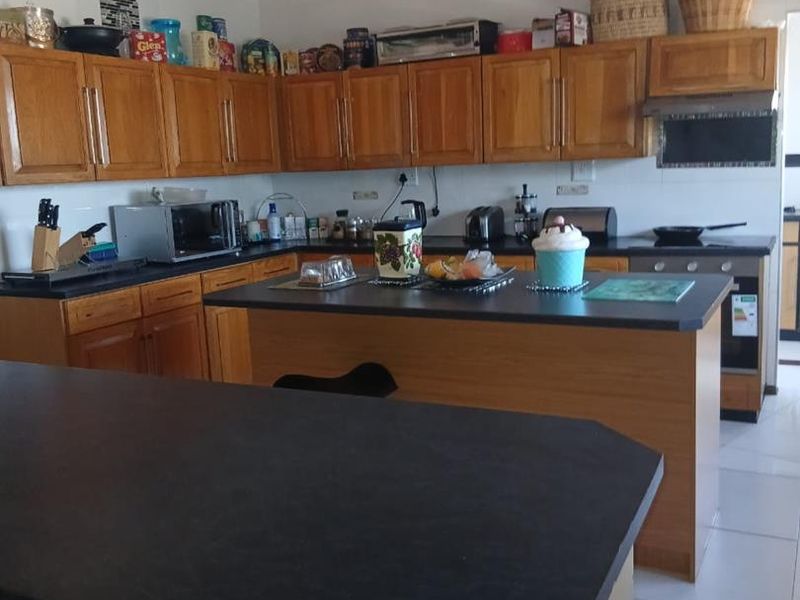 A functional kitchen featuring wooden cabinetry, dark laminate countertops, a central island, and built-in cooking appliances with tiled flooring.