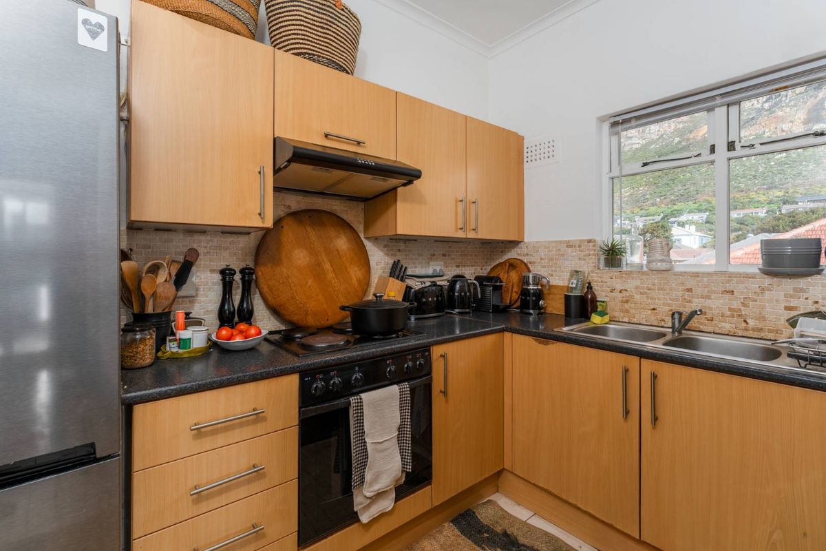 Compact kitchen featuring light wood cabinetry, dark laminate countertops, a built-in oven with extractor fan, and a double stainless steel sink.
