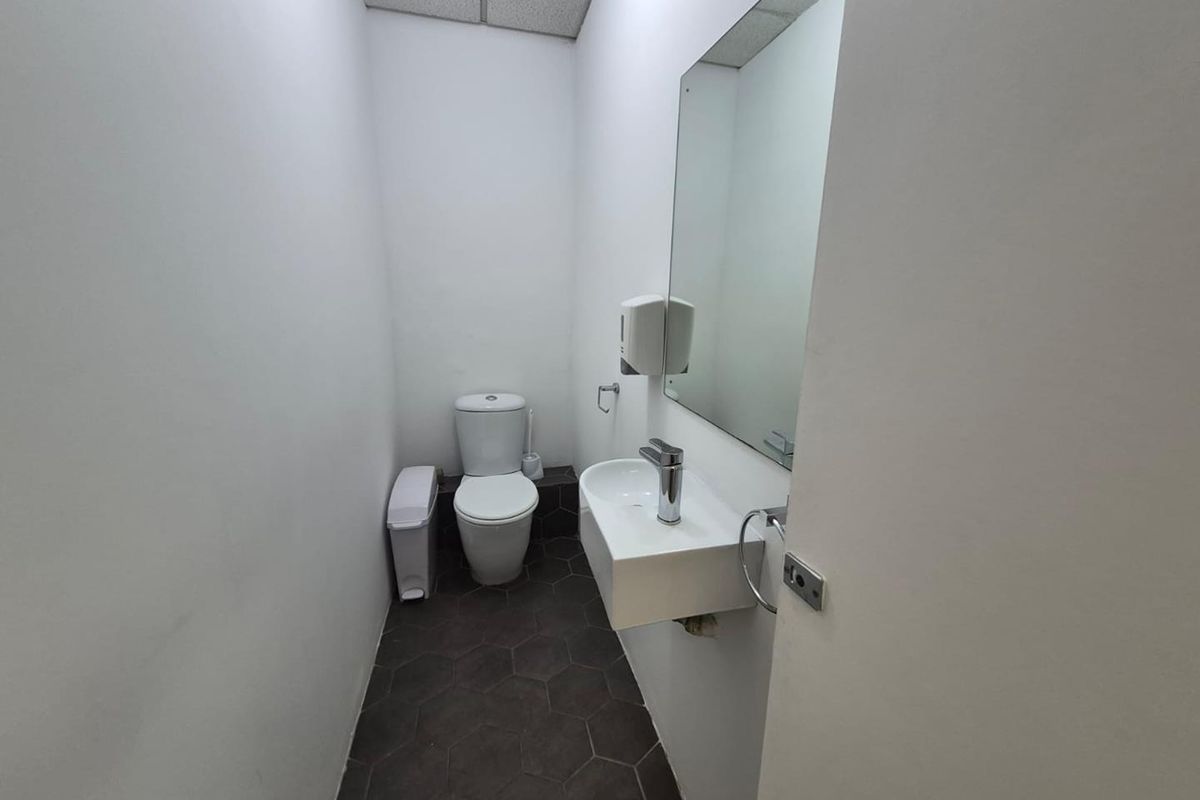 A clean, compact office restroom featuring a wall-mounted basin, modern faucet, toilet, and dark hexagonal floor tiles.