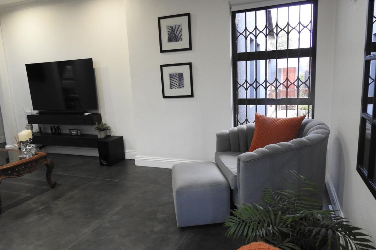 A modern living room featuring large format dark floor tiles, crisp white walls, and a secure window with a decorative metal security gate.