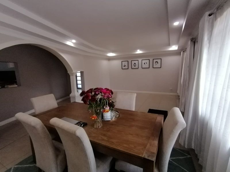A spacious dining area featuring a decorative arched entryway, recessed ceiling with integrated downlights, and neutral tiled flooring.
