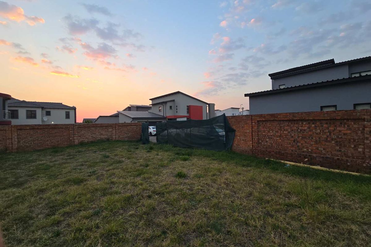 A vacant residential plot featuring a brick boundary wall and established grass lawn, situated within a developed neighborhood.