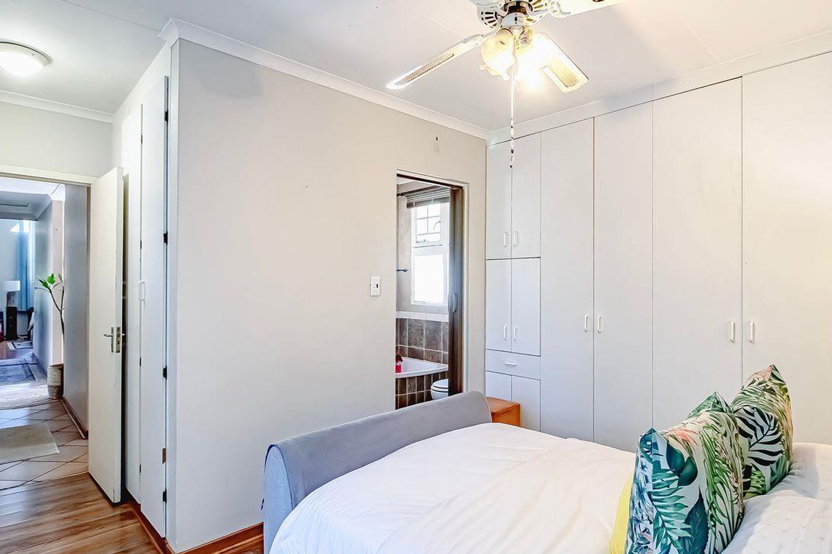 Bedroom featuring built-in cupboards, a ceiling fan, and an en-suite bathroom, with a view into the adjacent hallway.