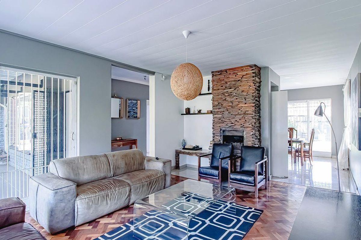 Spacious living room featuring a prominent stacked stone fireplace, classic parquet flooring, and large sliding glass doors leading to an outdoor patio area.