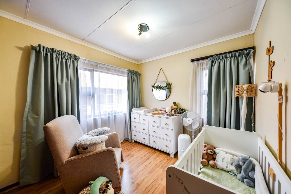 A cozy bedroom featuring laminate flooring, neutral wall tones, and dual windows with curtain rods, providing a bright and functional space.