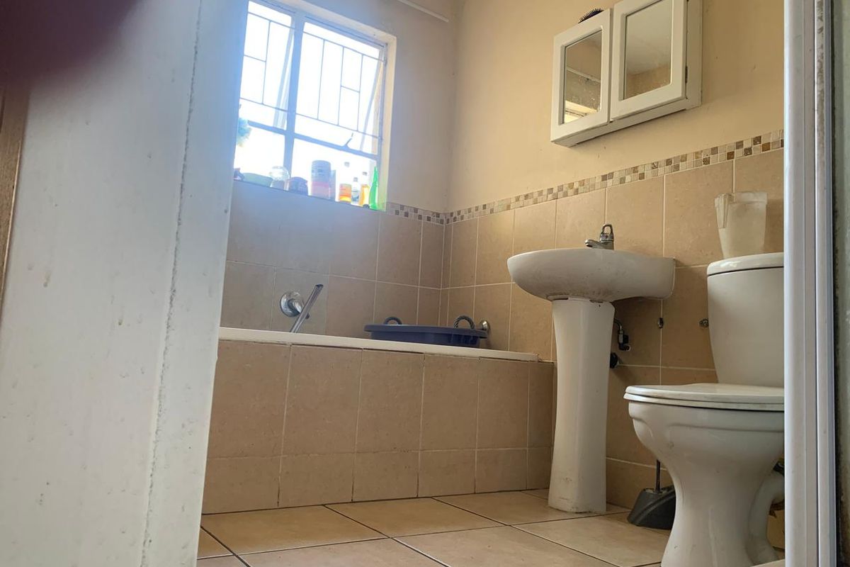 A functional bathroom featuring a pedestal basin, toilet, and built-in bathtub with tiled finishes and a wall-mounted medicine cabinet.