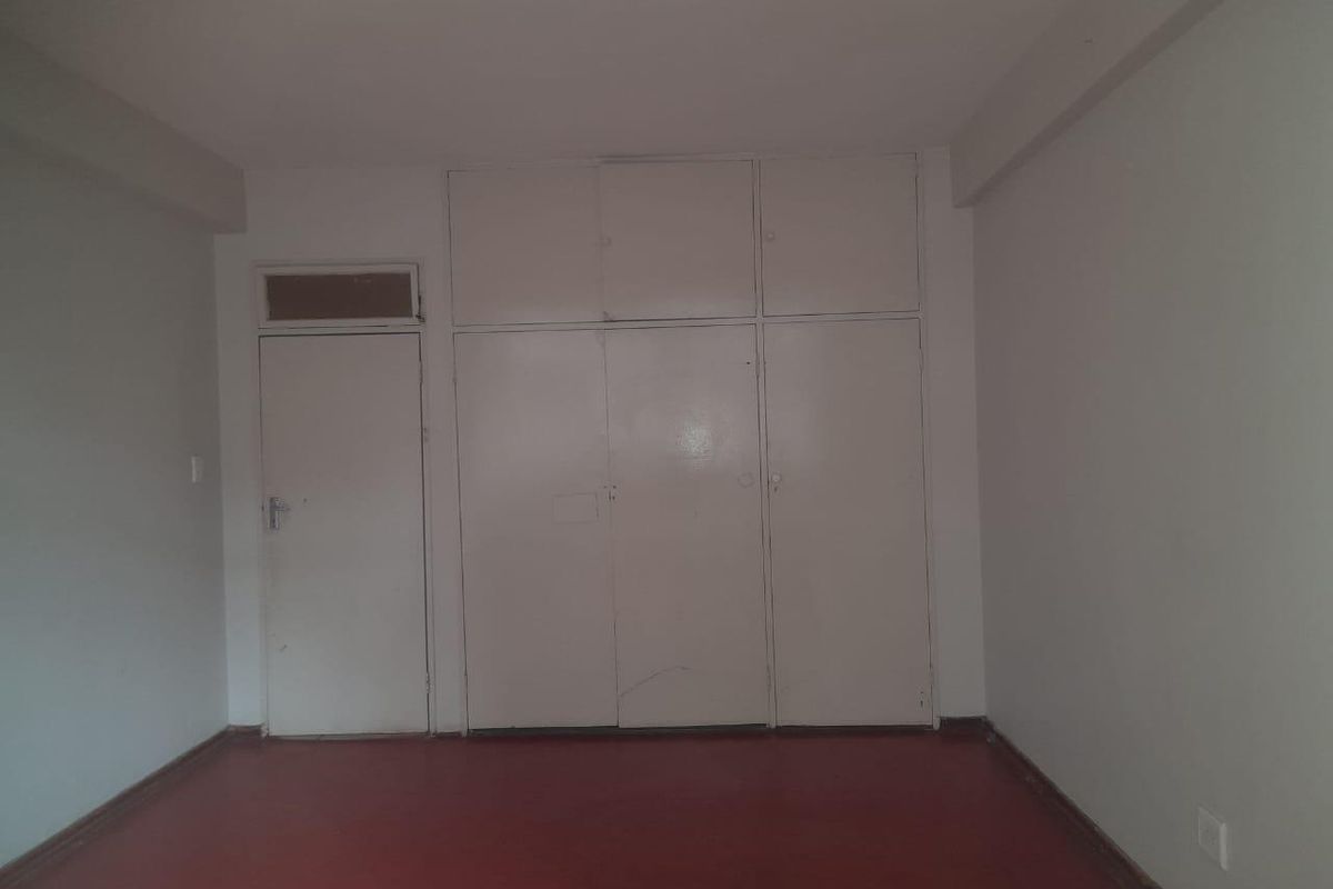 A vacant bedroom featuring built-in storage cupboards and a simple interior door, providing a blank canvas for renovation.