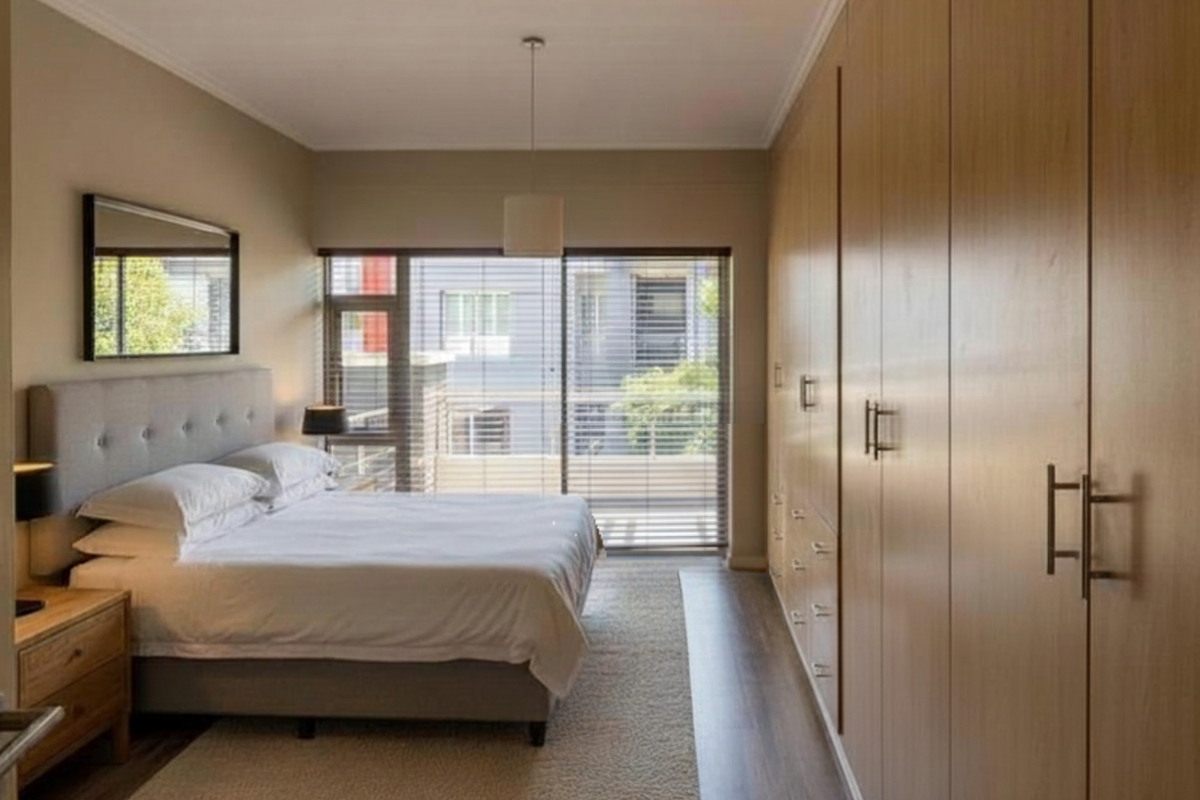 A well-maintained bedroom featuring extensive built-in wooden cabinetry, neutral wall tones, and large sliding glass doors leading to an outdoor balcony area.
