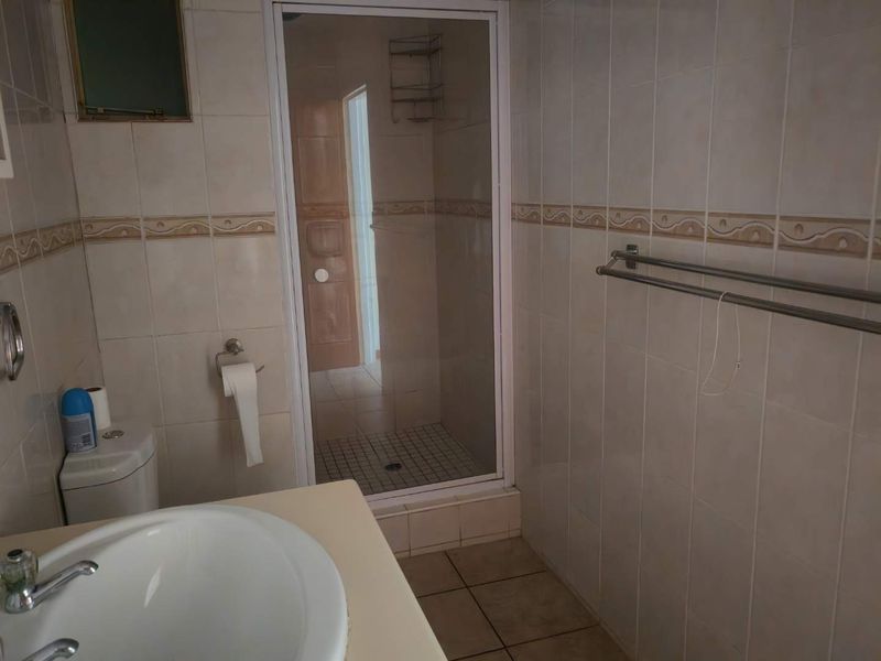 A functional bathroom featuring a shower enclosure, vanity basin, and toilet, finished with neutral ceramic wall and floor tiles.