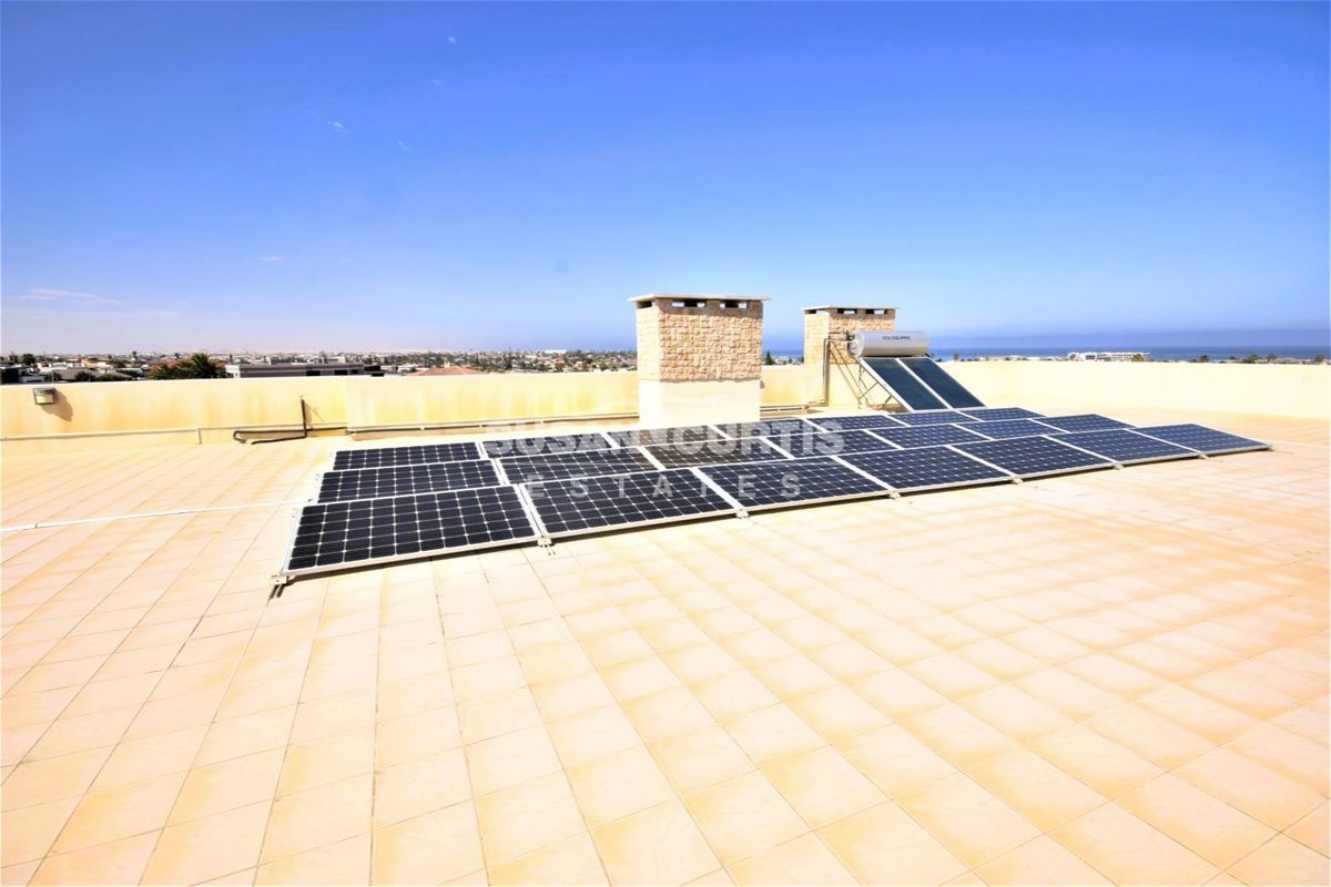 A spacious rooftop terrace featuring a solar panel array and solar water heating system, offering expansive views of the surrounding area.