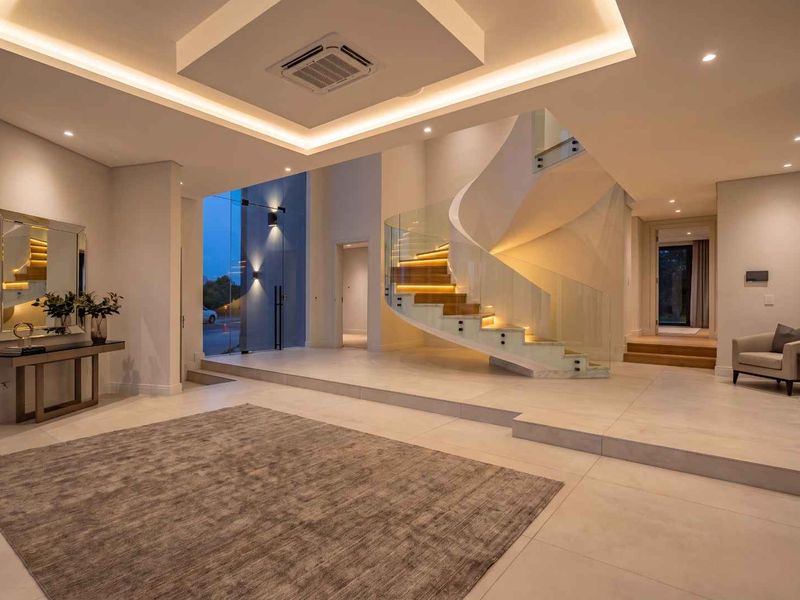 Grand entrance hall featuring a striking spiral staircase with glass balustrades, modern recessed ceiling lighting, and elegant tiled flooring.