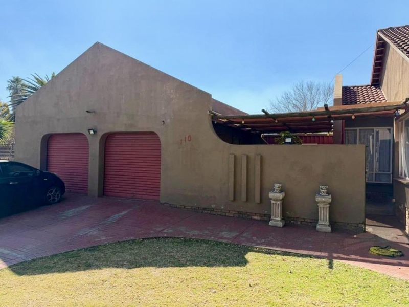 Front elevation of the property featuring a double garage with roller shutter doors, a paved driveway, and a covered patio area.