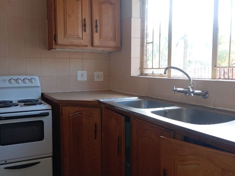 A dated kitchen featuring wooden cabinetry, a double bowl stainless steel sink, and a freestanding stove with tiled splashbacks and flooring.