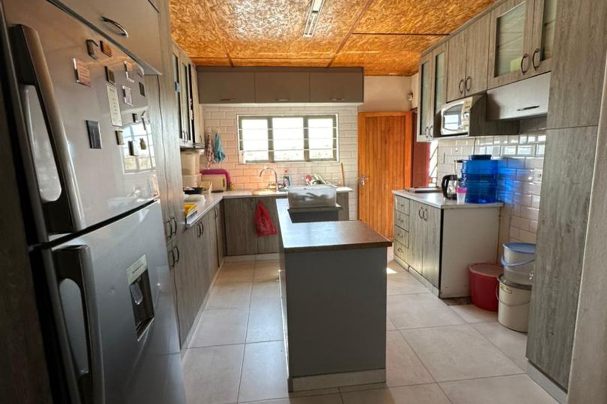 A functional kitchen featuring grey cabinetry, tiled flooring, a central island, and a distinctive exposed wood-chip board ceiling.