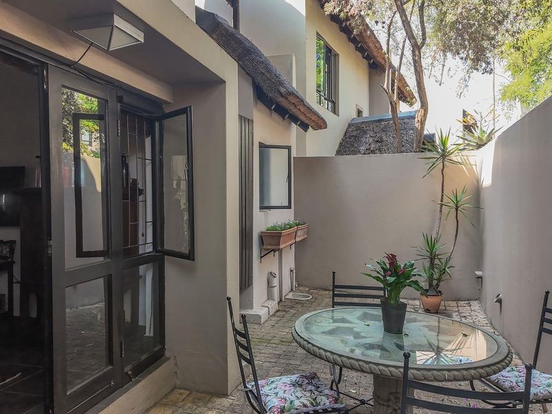 A private, paved courtyard patio area featuring a thatched roof overhang, accessible through large glass doors, providing a quiet outdoor living space.